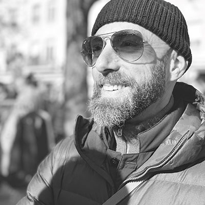 black and white photo of Mark Brinda standing outside wearing a beanie and sunglasses