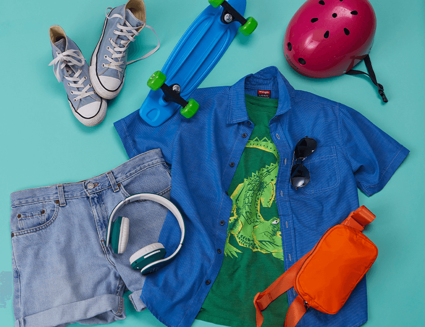 Assorted leisure items including a skateboard, a helmet, a pair of sneakers, a blue shirt over a graphic t-shirt, denim shorts, sunglasses, headphones, and a bright orange bag arranged on a teal background.