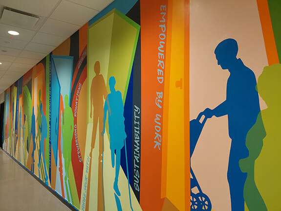 Photograph of the mural in the hallway from the right at GESMN's career campus. The mural is very colorful and shows people walking through doorways.